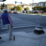 Man_and_delivery_robot_waiting_at_pedestrian_crosing_in_Redwood_City_California