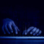 Cyberattack and internet crime, hacking and malware concepts. Digital binary code data numbers and secure lock icons on hacker’ hands working with keyboard computer on dark blue tone background.