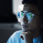 Code,  Asian man  and reflection in glasses, focus and programming for cyber security, hacking and modern office. Japan, male employee with eyewear and IT specialist coding, programming and thinking
